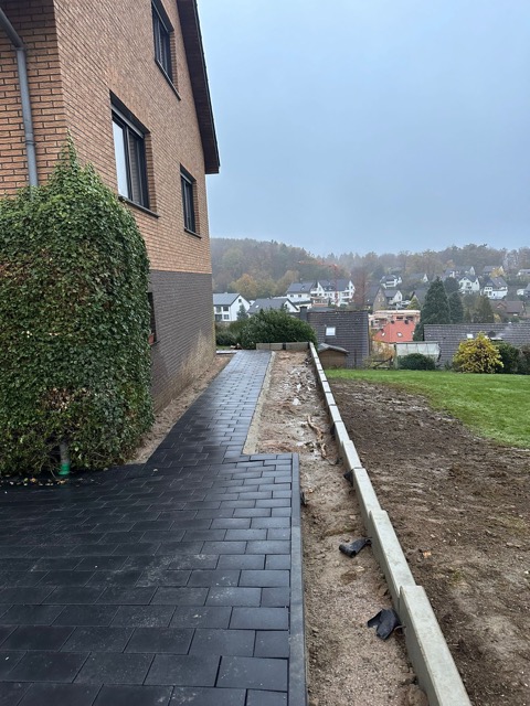 Ziegelhaus mit neuem Pflasterweg, Betonrand und Rasen; ruhige, neblige Herbststimmung.