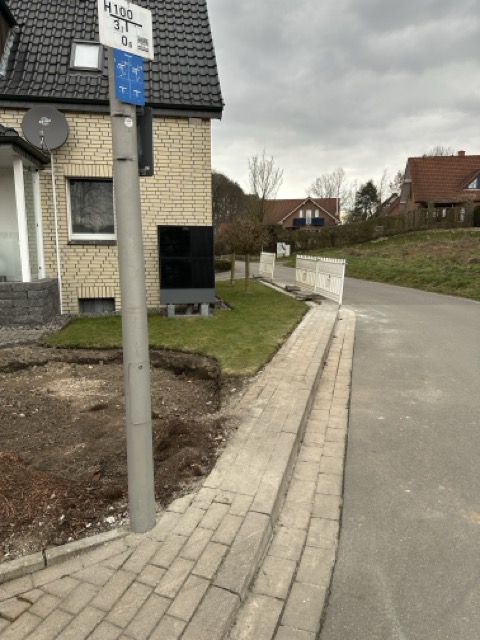 Ein Haus mit heller Klinkerfassade, dunklem Dach und kleinem Garten in einem ruhigen Wohngebiet.