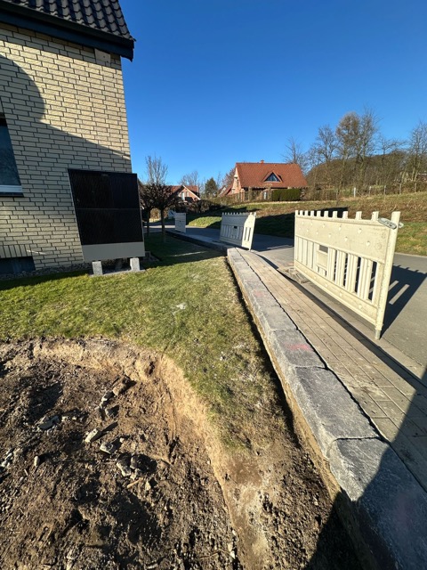 Wohngebiet mit hellem Backsteingebäude, Baustelle im Vordergrund und Betonabsperrungen bei sonnigem Wetter.