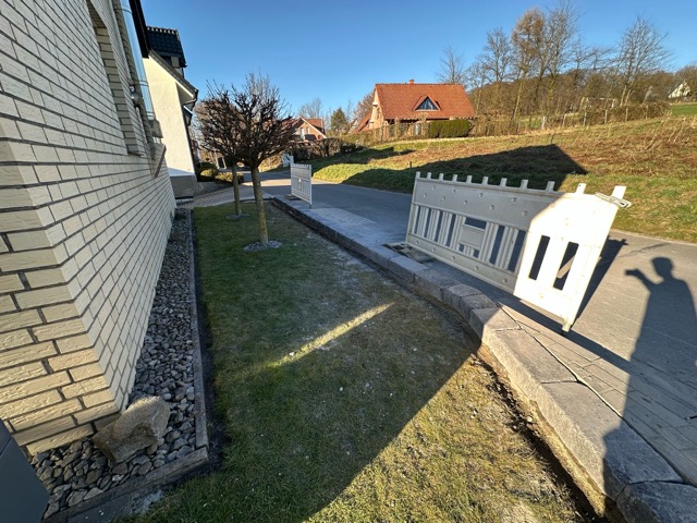 Ruhige Wohngegend mit weißem Backsteinhaus, kahlen Bäumen und sonnigem Wetter.