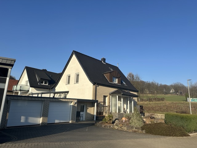 Ein beige Einfamilienhaus mit dunklem Dach und Doppelgarage in ruhiger, sonniger Wohngegend.