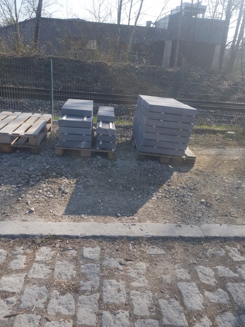 Gestapelte Betonplatten auf Holzpaletten auf einer ruhigen Baustelle mit bewaldetem Hintergrund.