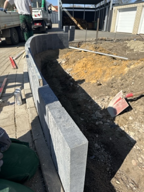 Eine Baustelle mit einer teilweise errichteten grauen Betonmauer und verstreuten Werkzeugen im Freien.
