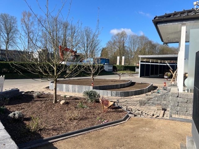 Moderner Garten mit blattlosem Baum, grauen Steinbeeten, gepflastertem Weg und modernem Gebäude.