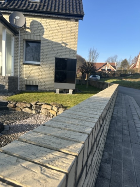 Ein modernes Haus mit heller Ziegelfassade, Satellitenschüssel und Klimaanlage, umgeben von gepflegtem Rasen.