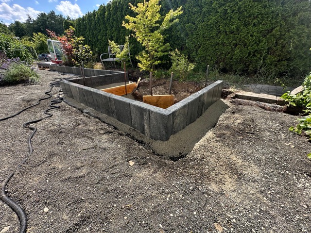 Ein L-förmiges Hochbeet aus Betonblöcken mit frisch gepflanzten Sträuchern in einem sonnigen Garten.